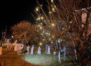 Jardín con siluetas de cartón de los Reyes Magos y muñeco de nieve, con luces navideñas en el árbol, de Marisa Álvarez